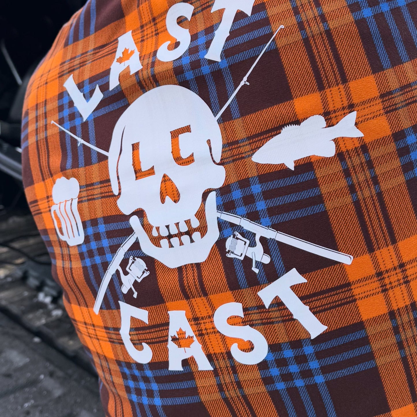 Person wearing an orange and blue plaid shirt with 'Last Cast' logo, standing outdoors.